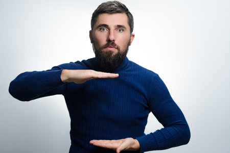 A bearded man in a blue sweater gestures with his hands, creating a space as if holding an invisible object against a light background.の写真素材