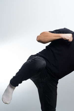 A person wearing a dark shirt and pants delivers a front kick while wearing white socks against a plain background. Focus on the dynamic movement.の写真素材
