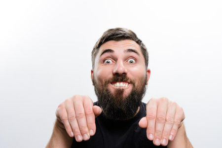 A bearded man against a white background makes a playful, silly face and gesture with his hands, conveying humor and lightheartedness.の写真素材