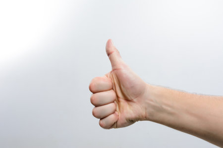 A close-up of a hand giving a thumbs up sign against a simple, uncluttered background. The gesture signifies approval, positivity, or agreement.の写真素材