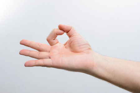 Close-up of a hand forming the 'okay' gesture with thumb and index finger touching. The other fingers are extended against a clean white backdrop.の写真素材