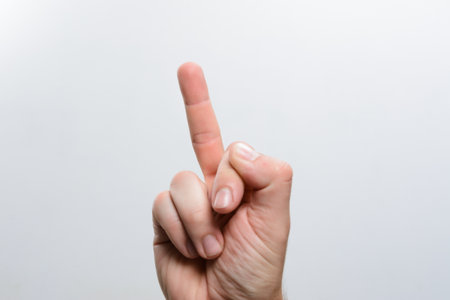 A close-up of a hand making a gesture with an extended finger against a simple, light gray backdrop. The focus is on the hand and its position.の写真素材