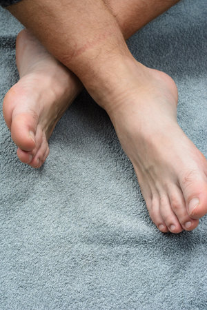 Close-up of bare feet resting on a soft, textured gray towel. The feet are crossed at the ankles, suggesting relaxation and comfort.の写真素材