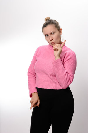 A woman wearing a pink top and black leggings makes a quiet gesture with her finger to her lips, suggesting secrecy.の写真素材