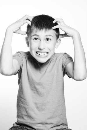 A black and white close-up shot of a young boy with a frustrated expression, hands gripping his head. He appears stressed or angry. The image is simple and impactful.の写真素材