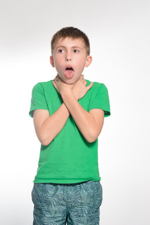 A photo of a boy experiencing respiratory distress. He is wearing a green shirt and patterned shorts. The expression on his face conveys urgency and discomfort.の写真素材