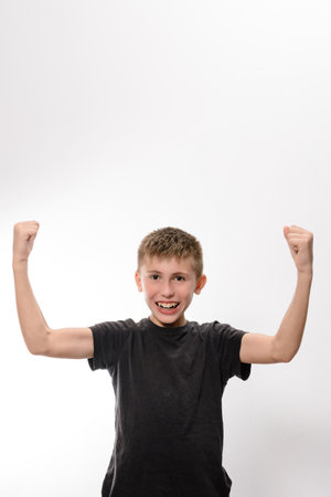A young boy, wearing a dark gray t-shirt, celebrates triumphantly with both arms raised in the air....
