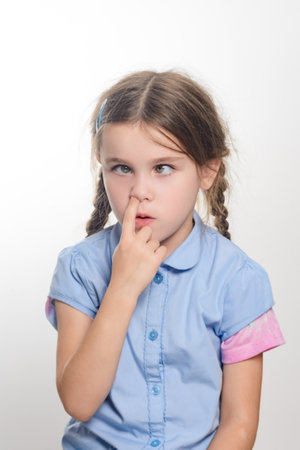 A closeup shot of a girl with pigtails, wearing a light blue shirt, playfully touching her nose with...