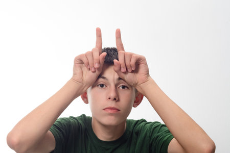 A portrait of a teenage boy playfully making horns on his forehead. He's wearing a dark green shirt and has a neutral expression.の写真素材
