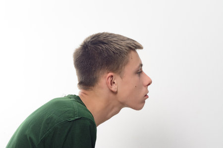 A close-up profile shot of a teenage boy. He has short, neatly styled brown hair and is wearing a simple dark green t-shirt. The background is plain white.の写真素材