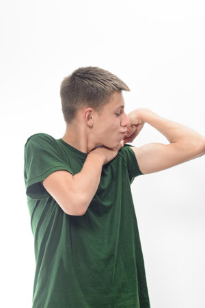 A young man in a green t-shirt playfully shows off his bicep. He's looking at his arm with a slightly amused expression. The photo is taken against a plain white background.の写真素材