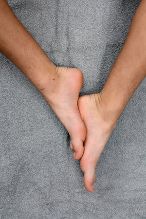 Close-up view of bare feet, ankles, and lower legs gently placed on a soft, gray textured fabric. The scene evokes a sense of calmness and relaxation.の写真素材