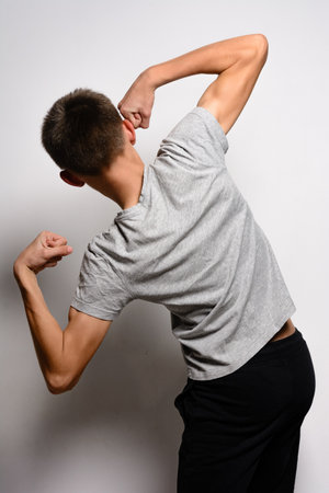 A rear view of a young man in a grey t-shirt and black pants flexing his biceps. He's posed against a plain white backdrop.の写真素材