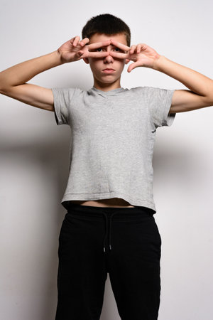 A young person, wearing a gray shirt and black pants, playfully covers their eyes with their hands. The photo is taken against a plain white background.の写真素材