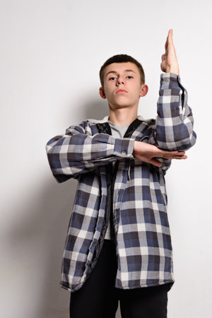 A young man with short brown hair poses in a blue and white plaid shirt. His arms are crossed, one hand raised slightly. He's looking directly at the camera. The background is plain white.の写真素材
