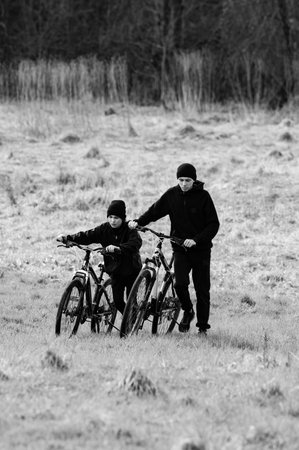 Brothers or friends walk their bicycles across a field, enjoying a sunny day. The monochrome image highlights the simplicity and camaraderie.の写真素材