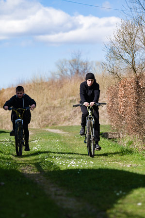 Two young people ride mountain bikes along a rural path, bathed in sunlight. The scene is peaceful and evokes a sense of freedom and outdoor adventure.の写真素材