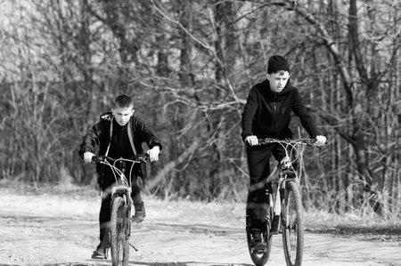 Black and white photo of two young boys biking down a country lane. The boys are wearing casual...