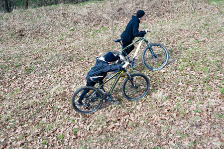 A high-angle shot captures two young boys working together to maneuver their mountain bikes up a steep, leaf-strewn incline. The scene evokes a sense of challenge and camaraderie.の写真素材