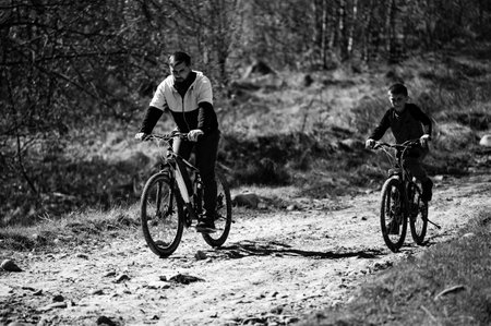 A heartwarming black and white image captures a father and son biking together on a dusty path. They...
