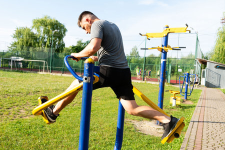 A bearded man performs a leg press on outdoor gym equipment. He's wearing athletic clothing, focused on his workout in a park setting.の写真素材