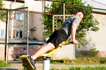 A young man performs a strength training exercise on outdoor gym equipment. He's focused and determined, enjoying a workout in the fresh air.の写真素材