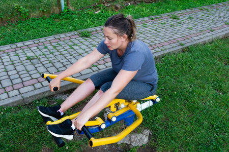 A woman uses an outdoor rowing machine in a park setting. She is focused on her workout, enjoying the fresh air and sunshine. A great way to stay active.の写真素材