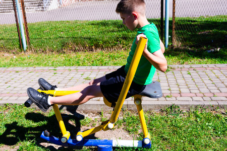A young boy uses outdoor gym equipment. He's focused on his workout. The sunny day and green surroundings enhance the scene of healthy activity.の写真素材