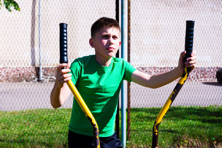 A young boy uses an outdoor fitness machine, focusing intently on his workout. The sun shines...