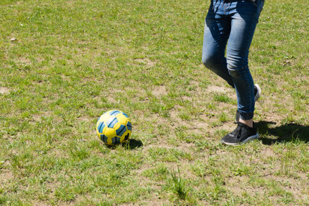 A soccer ball sits on a grassy field, with a person's legs and feet visible in the background, suggesting a moment of play.の写真素材