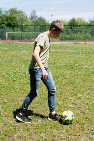 A young man practices his soccer skills on a grassy field. He is wearing jeans and a t-shirt. The sun is shining and the day is bright.の写真素材