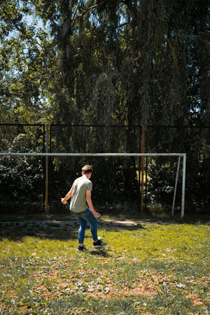 A person kicks a soccer ball on a grassy field near a soccer goal. The scene is outdoors, surrounded by trees and greenery under a bright sky.の写真素材