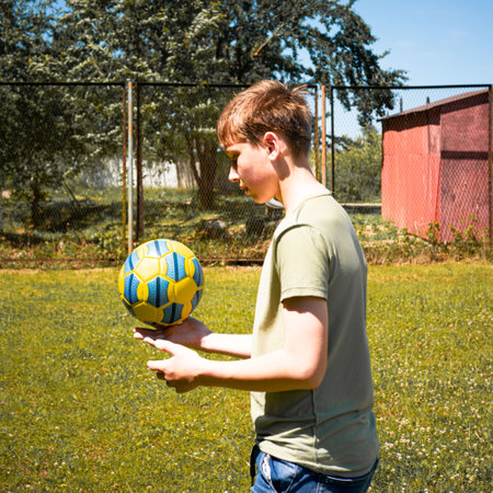 A young boy skillfully juggles a soccer ball in a grassy field. He's wearing a casual t-shirt and jeans. The sun shines brightly, creating a joyful summer scene.の写真素材