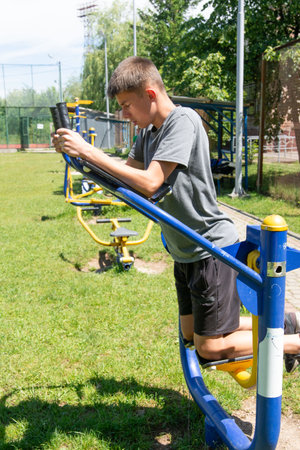 A young man uses public outdoor fitness equipment. He's focused on his workout on a sunny day in a park-like setting. The scene is bright and active.の写真素材