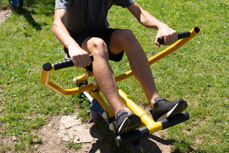Person exercising on outdoor fitness equipment in a park, strengthening leg muscles.