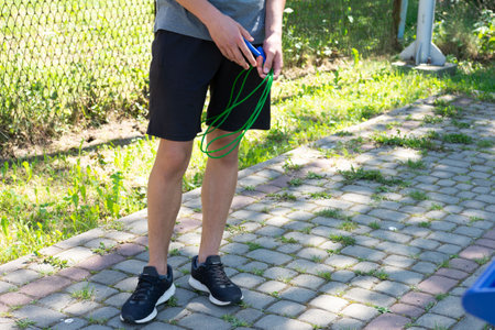 A man stands on a paved path, holding a jump rope. He's ready for a workout. The setting is outdoors, sunny and green.の写真素材