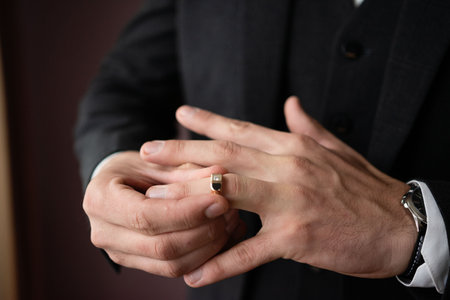Close-up view of a person's hands. One hand gently placing a ring onto the other. The image evokes feelings of commitment, and solemnity.の写真素材