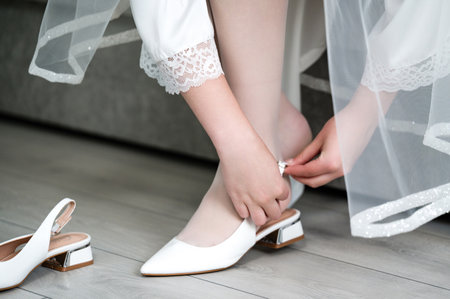 A bride delicately fastens her white heels, a moment of quiet preparation before her wedding. The shoes are elegant and stylish, reflecting the anticipation of the day.の写真素材