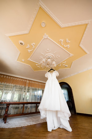 Elegant wedding dress hangs beneath an ornate chandelier in a beautifully decorated room.の写真素材
