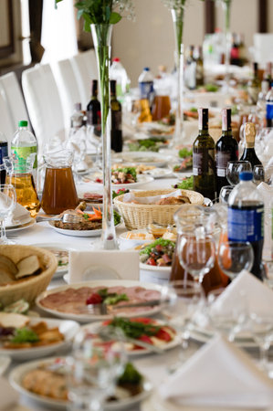 A long table is beautifully set for a formal event. A variety of dishes, drinks, and glassware are arranged, creating a lavish and inviting atmosphere.の写真素材