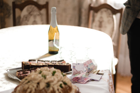 A table set for a celebration features various cakes, a bottle of sparkling wine, and some cash, suggesting a festive gathering with gifts or payments.の写真素材