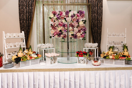 A beautifully decorated dessert table features an array of pastries, fruits, and candies. A stunning floral wall serves as a backdrop, enhancing the overall aesthetic.の写真素材