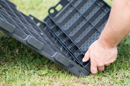 Close-up of hands assembling dark gray plastic components, possibly a tray or storage system. The setting is outdoors on a grassy lawn.の写真素材