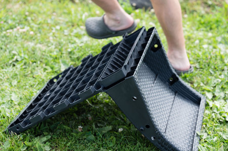 A person assembles a dark gray plastic storage container outdoors on a grassy area. The container is modular and appears to be made of interlocking panels.の写真素材