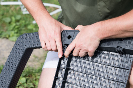 Close-up of hands assembling patio furniture. Dark gray woven plastic pieces are being connected. Outdoor setting.の写真素材