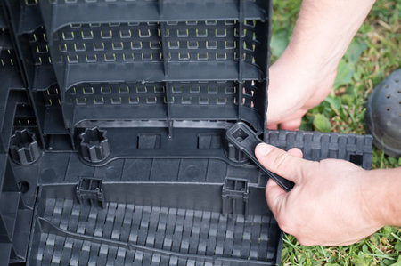 Close-up of hands assembling sections of a black plastic raised garden bed. The interlocking pieces create a modular system. Outdoor setting.の写真素材