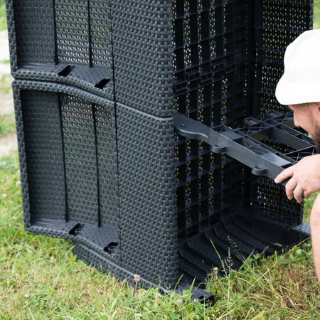 A person assembles dark gray plastic outdoor furniture. The pieces are woven-style and are being connected on a grassy lawn.の写真素材