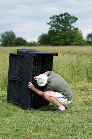 A person assembles black plastic patio furniture in a grassy field. The setting is outdoors, suggesting garden or yard work.の写真素材