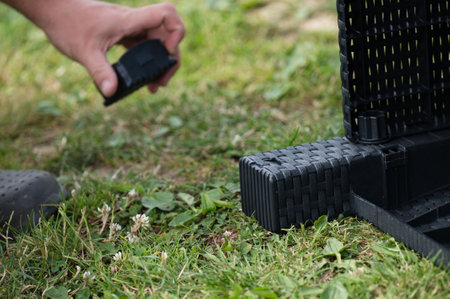 Close-up of a person's hand attaching a black plastic foot to a piece of outdoor furniture. The furniture has a woven design and is being assembled on a grassy surface.の写真素材