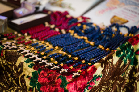 Close-up view of numerous beaded necklaces, each featuring a small cross, arranged neatly on a vibrant floral cloth. The necklaces are predominantly blue and red.の写真素材